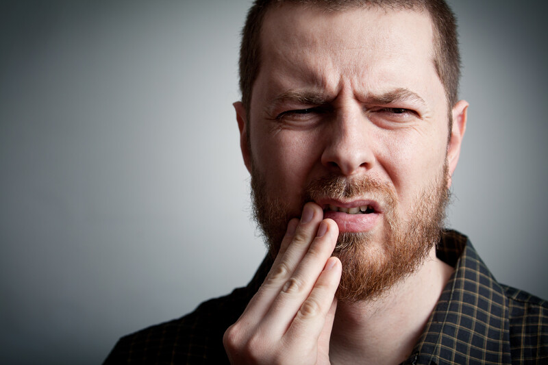 Man holding his mouth in pain due to a knocked-out tooth, indicating a dental emergency requiring immediate attention.